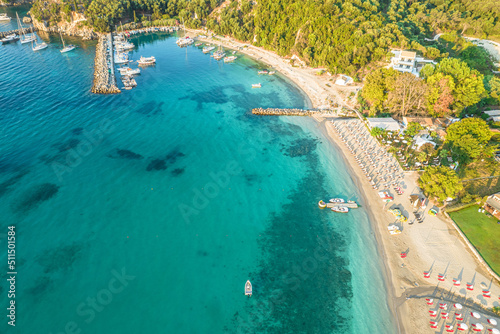 Port with boats, cruise ship and colorful houses of seaside town of Parga. Beach with tourist people, blue, turquoise sea water. Summer vacations and travel concept. Greece. Aerial, drone view