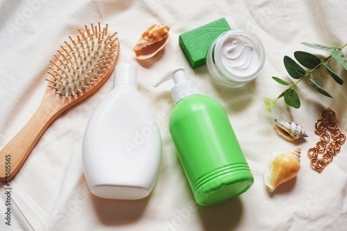 Flat lay still life beauty photography. Wooden comb, white shampoo bottle, green liquid soap package, face cream. Summer toiletries essentials for hair and skin care