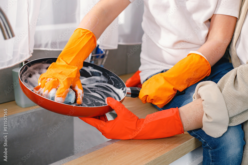 Cropped photo of two pair of hands washing a frying pan in a kitchen Cropped photo of two pair of hands washing a frying pan in a kitchen
