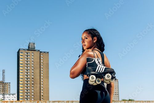 Photos Rear view of a young woman carrying her roller skates, urban background