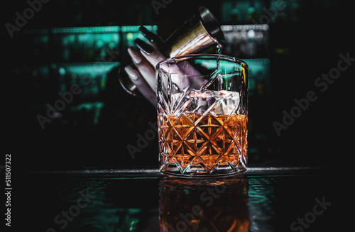 Fotografia, Obraz woman hand bartender pouring whiskey into a glass with ice at the bar