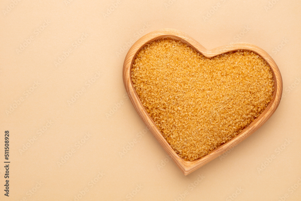 Brown sugar in heart wooden bowl shape on pasttel background.