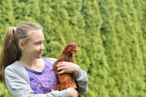 A joyful girl holds a chicken in her hands and hugs her.