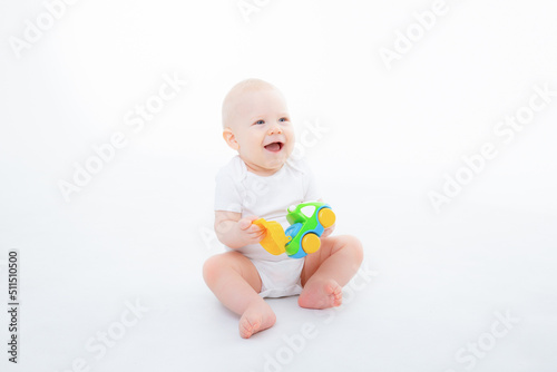baby boy in a white bodysuit is sitting playing  with toy cars on white background