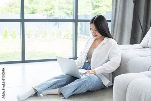 beautiful young asian woman in white shirt using laptop sitting on floor at bright modern interior