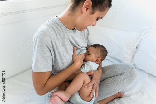 Happy mother breastfeeding her little baby on bed - Family and Maternity concept