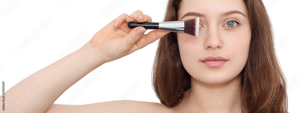 A beautiful yound woman with blue eyes is holding make up brush in front of her eye, close up, banner.