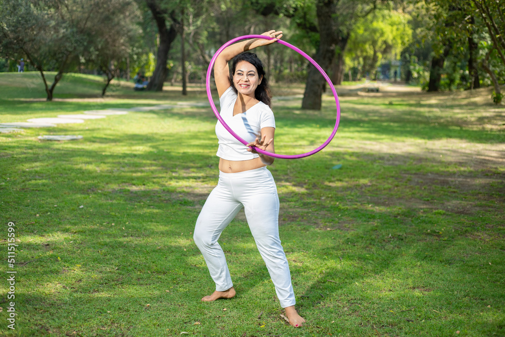 Young sporty Indian woman exercise with ring or hula hoop having fun in summer park outdoor, acrobatic Female gymnastic Sport and fitness activity. Aerobics. Young sporty Indian woman exercise with ring or hula hoop having fun in summer park outdoor, acrobatic Female gymnastic Sport and fitness activity. Aerobics.