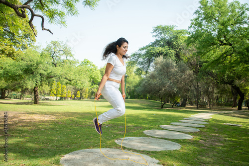 Young indian fitness woman wearing white sportswear skipping rope at park , Asian female Jumping exercise outdoor. photo