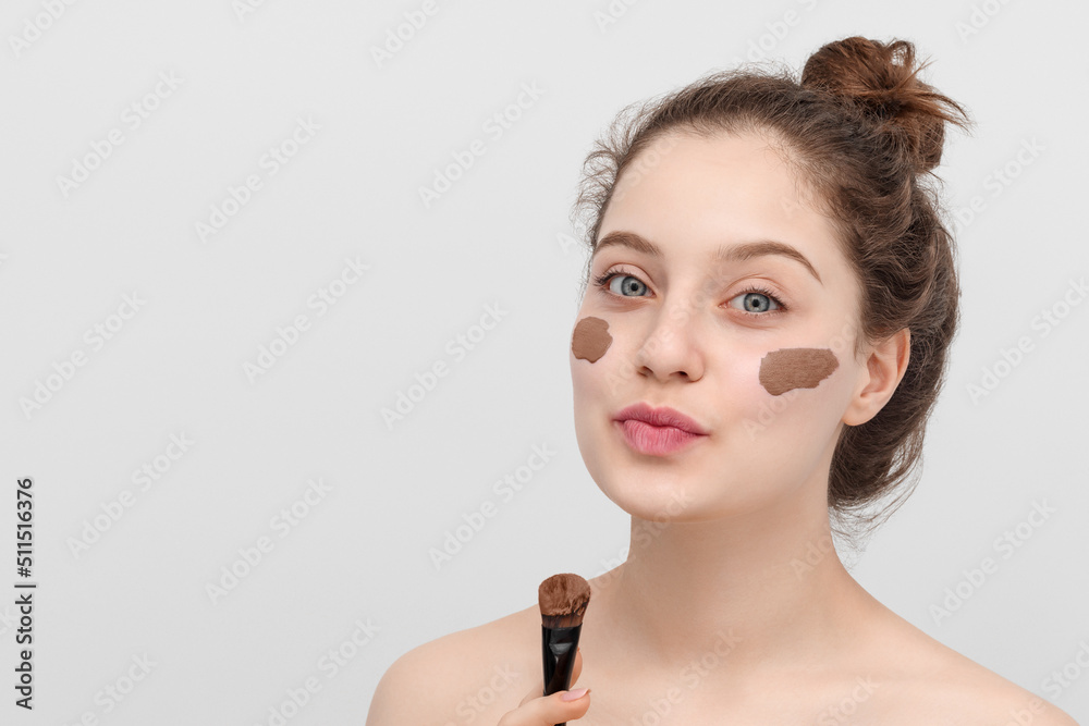 Portrait of a beautiful young woman apply clay face mask with a brush. Blue eyes, brown curly hair in a bun. Portrait of a beautiful young woman apply clay face mask with a brush. Blue eyes, brown curly hair in a bun.