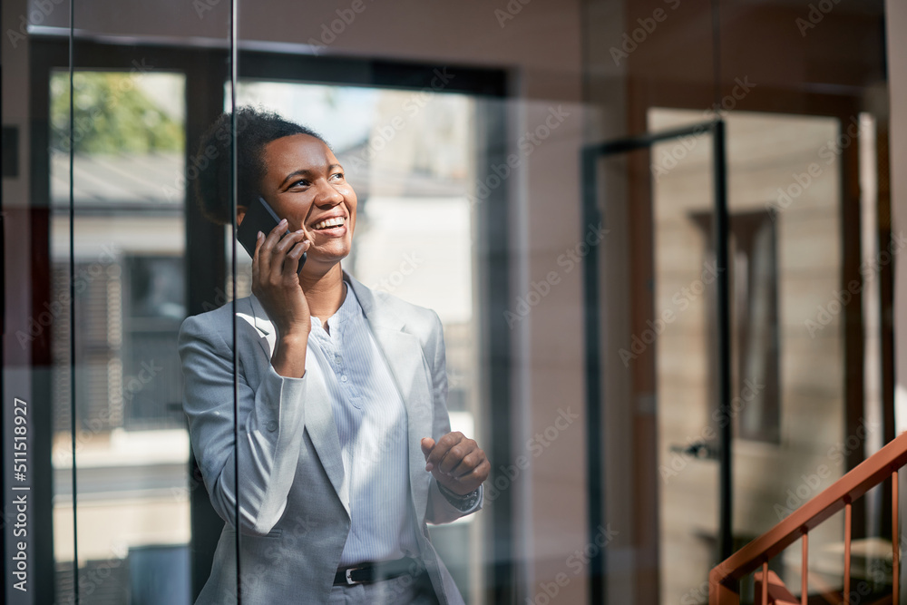 Cheerful black businesswoman talking on the phone in hallway. Cheerful black businesswoman talking on the phone in hallway.