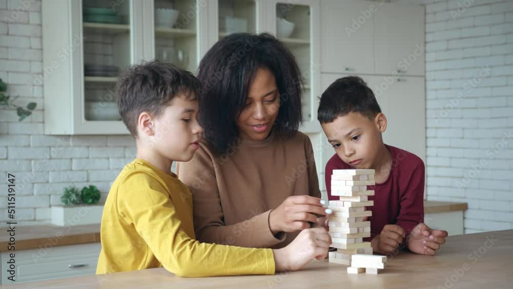 African American mom with kids playing board game, laughing after high toy wooden blocks tower falling. Family spending time together at home. Enjoying educational games during lockdown or day off African American mom with kids playing board game, laughing after high toy wooden blocks tower falling. Family spending time together at home. Enjoying educational games during lockdown or day off