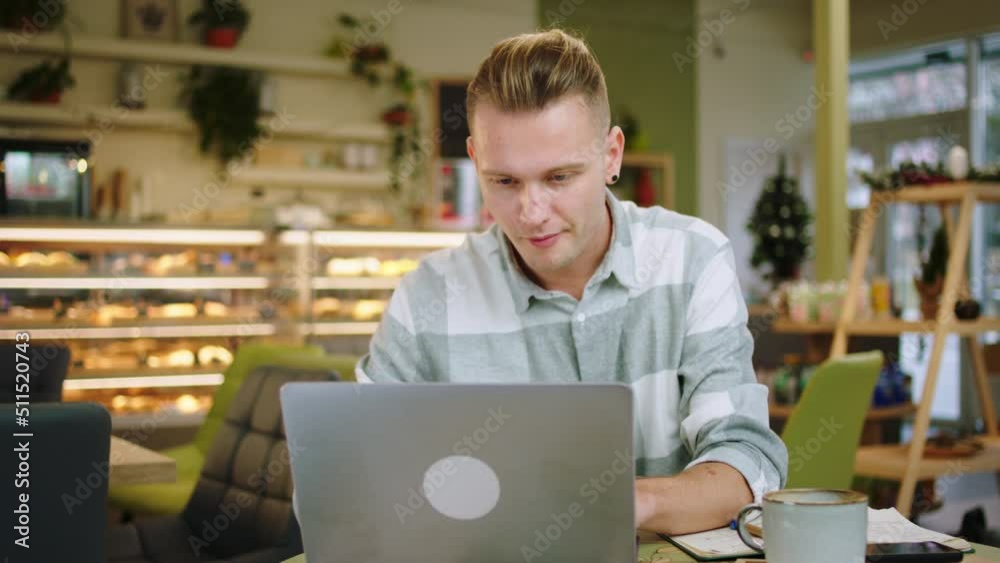 Handsome man Woking online on his laptop while drinking his coffee in a modern coffee shop he concentrated looking at the laptop Handsome man Woking online on his laptop while drinking his coffee in a modern coffee shop he concentrated looking at the laptop