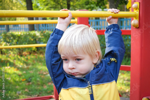 Portrait of two years old child boy at colourful playground area. Autumn public park. Little blond boy playing outdoors. Happy kid on a jungle gym. Sport and lifestyle Concept