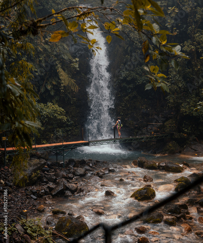 Woman on a small crossing bridge admiring a waterfall in the forest