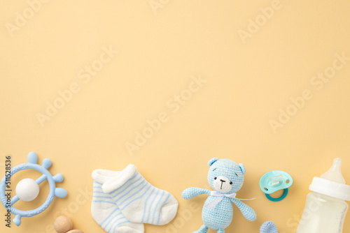 Baby boy concept. Top view photo of knitted teddy-bear toy blue rattle milk bottle pacifier and tiny socks on isolated pastel beige background with copyspace photo