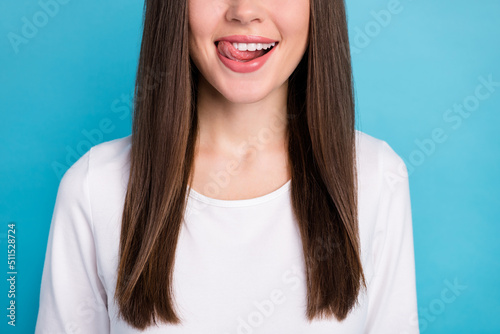 Cropped view portrait of attractive cheerful funny girl licking lips tasty balm lipstick isolated over bright blue color background