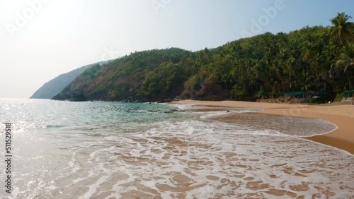 4K Wide angle shot of sea waves on the shore of a tropical beach at Kakolem beach in South Goa, India. Sea waves on the shore of a tropical beach island. Sea waves at the beach on a remote island.  photo