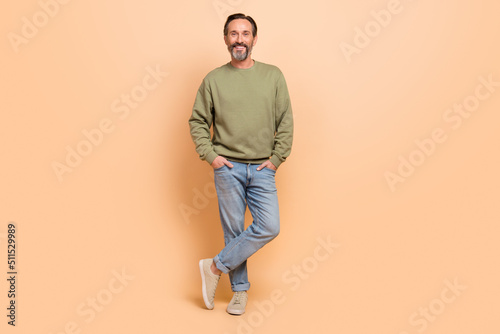 Full length body size view of attractive cheerful man holding hands in pockets isolated over beige pastel color background