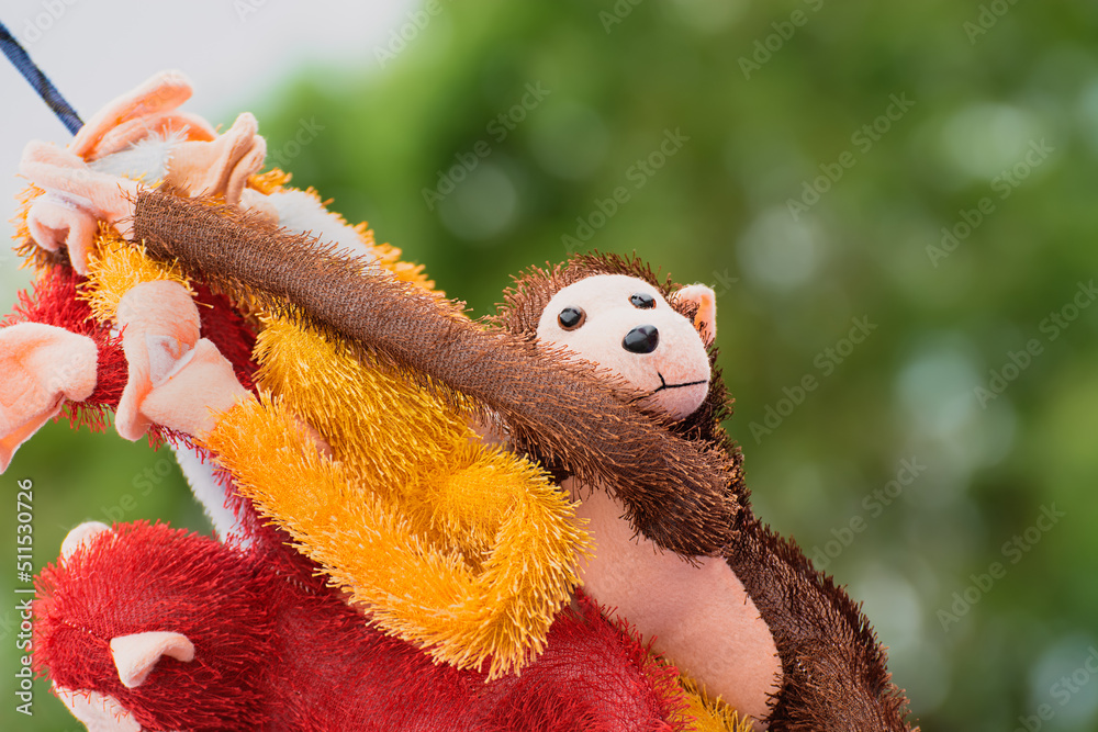 A naughty soft toy monkey dangling with other toys attracts the attention of kids . The background of soft diffused green trees makes the toys stand out prominently.