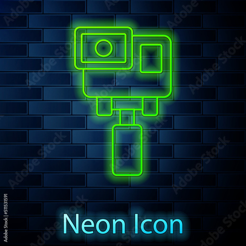 Glowing neon line Action extreme camera icon isolated on brick wall background. Video camera equipment for filming extreme sports. Vector