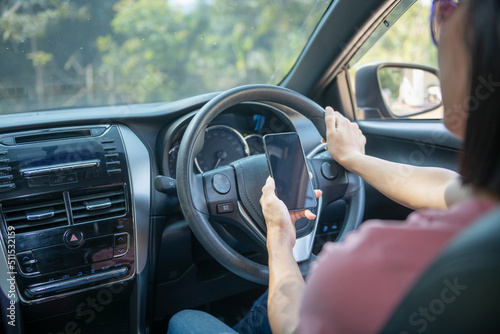 Mockup image of a woman holding and using mobile phone with blank screen while driver a car, for GPS, Lifestyles photo in car, Interior, front view. With woman hand holding phone. © sutlafk