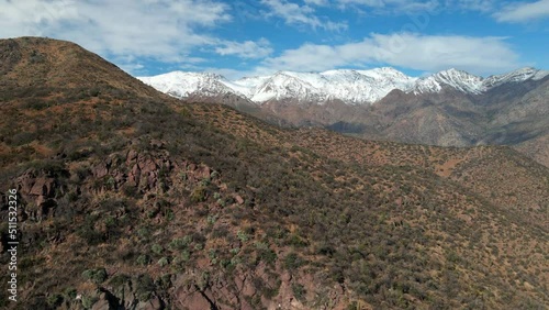 Aerial orbit with parallax effect at Morro Las Papas, San Carlos de Apoquindo Park, Las Condes, Santiago, Chile. Snowy mountain range in the background photo