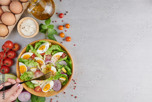 Girls' hands holding healthy vegetarian breakfast bowls flat-lay. Healthy salad of fresh vegetables - tomatoes, egg, Onion. high angle view of a nutritious vegetable salad with boiled egg slices.