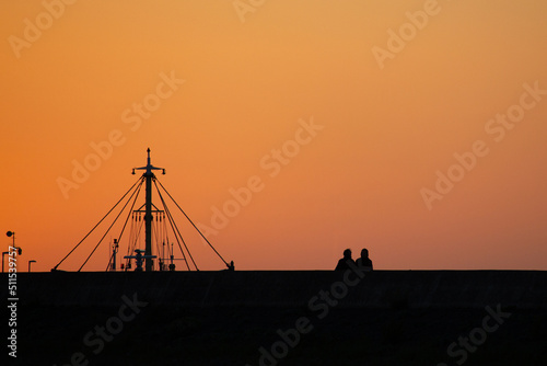 silhouette of a couple at beach at sunset with sailboat in background