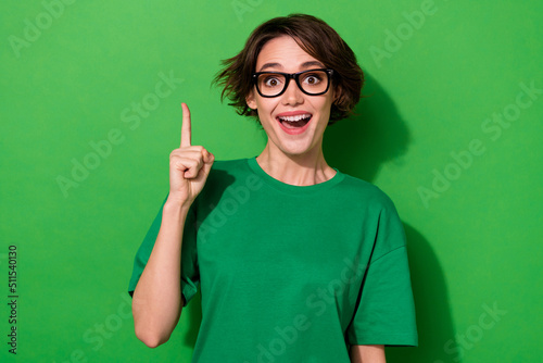 Photo of pretty excited young lady dressed casual t-shirt eyewear pointing empty space isolated green color background