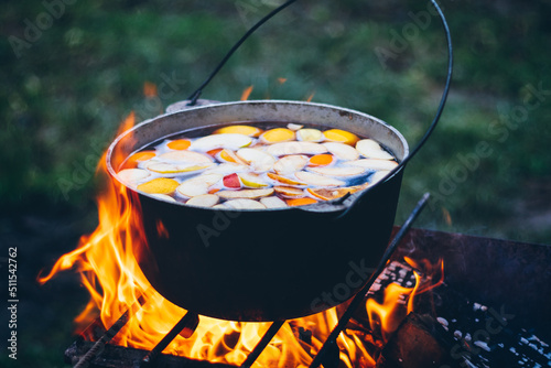 Fruit compote is cooked in a cauldron on the fire, outdoors. 