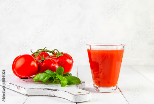 Fresh tomato juice, tomatoes and basil on a light wooden background. Copy space