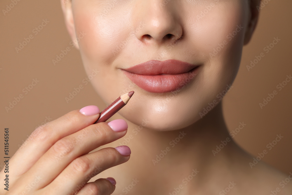 Young woman with beautiful nude lip pencil on beige background, closeup