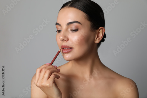 Foto Pretty young woman applying beautiful nude lip pencil on grey background