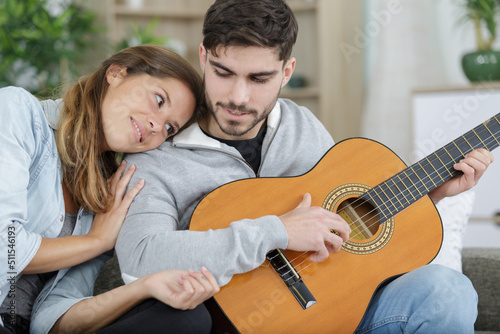 couple sitting and embracing on couch while man playing guitar