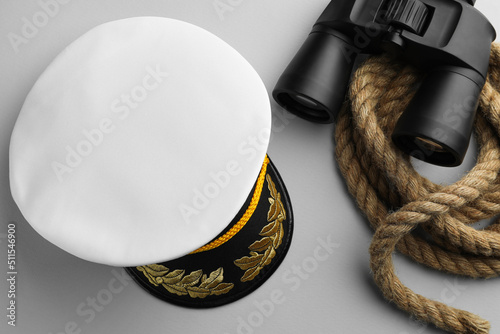 Peaked cap, rope and binoculars on light grey background, flat lay photo