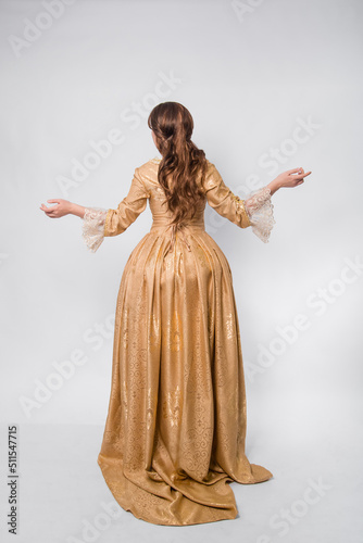 Full length portrait of a woman in a gold dress in the style of the rococo era, standing with her back forward and posing isolated on a white background.