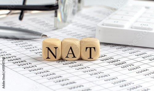 wooden cubes with the word NAT Network Address Translation on a financial background with chart, calculator, pen and glasses, business concept.