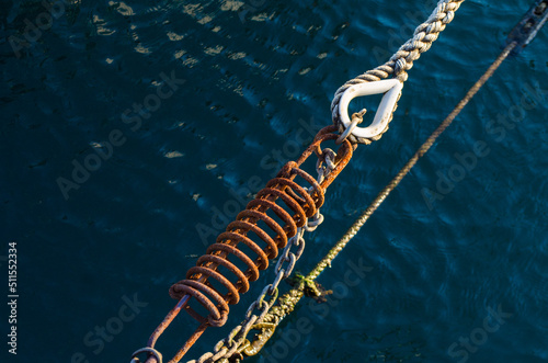 La molla arrrugginita di un tirante per barche sospesa sul mare blu di un porto