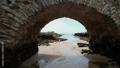 Flythrough underneath a rocky bridge revealing Santa Marta Lighthouse in Cascais, Portugal photo