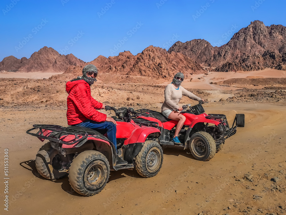 Adult man and woman dressed in arafatkas sit on quad bikes against the backdrop of stone mountains in the Echo Valley near Sharm El Sheikh, Egypt. Couple of tourists on ATVs in the Sinai Desert Adult man and woman dressed in arafatkas sit on quad bikes against the backdrop of stone mountains in the Echo Valley near Sharm El Sheikh, Egypt. Couple of tourists on ATVs in the Sinai Desert