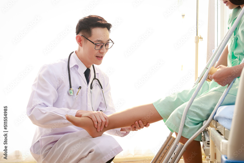 Asian male doctor examining the legs of a female patient sitting on a