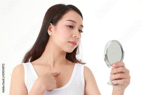 Beautiful Asian woman holding a mirror to look at pimples on her chest. She was very stressed. Beauty concept, beautification, beauty skin care. white background © SUPERMAO