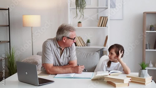 Family study. Home lesson. Private class. Middle-aged father helping little daughter with homework explaining task at modern workplace interior. photo