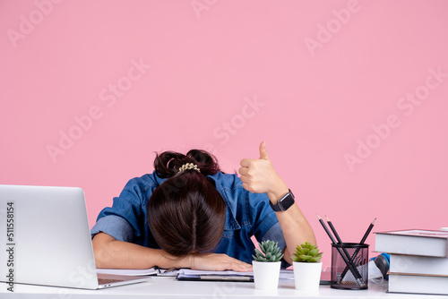 Young tired Asian woman wearing a casual shirt. She siting sleep laid her head down on white office desk isolated on a pink background photo