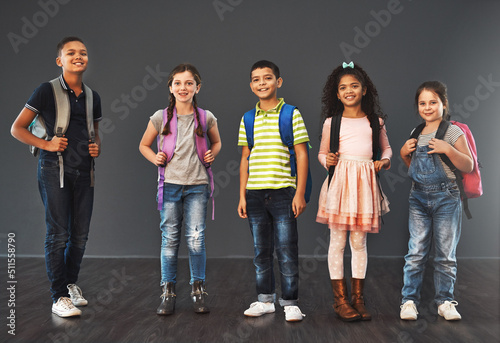 Little people, big day. Studio portrait of a diverse group of kids carrying their school backpacks against a gray background.