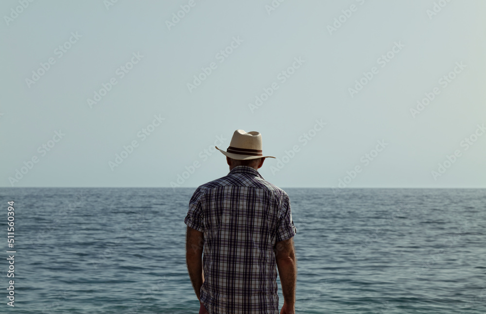 Rear view of adult man in shirt and hat against sea and sky