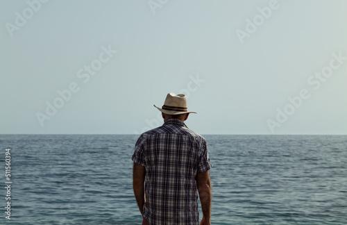 Rear view of adult man in shirt and hat against sea and sky © WeeKwong