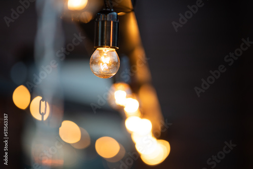 Glowing yellow lightbulb hanged on ceiling against black wall. Bokeh background.