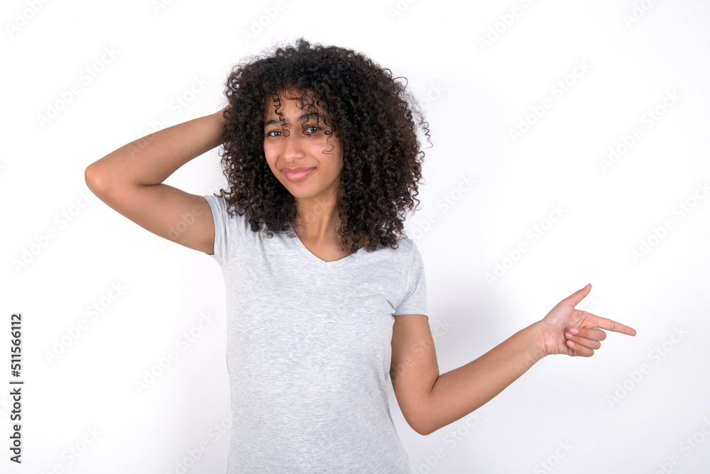 Surprised Young beautiful girl with afro hairstyle wearing grey t-shirt over white wall pointing at empty space holding hand on head Surprised Young beautiful girl with afro hairstyle wearing grey t-shirt over white wall pointing at empty space holding hand on head